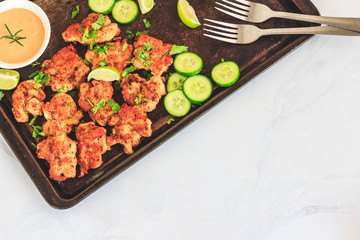 Chicken Fritters on a Dark Baking Tray with Cucumber Slices, Bell Pepper Cubes and Lemon, Garlic Aioli in the Bowl, Top View Food, Negative Space, White Background