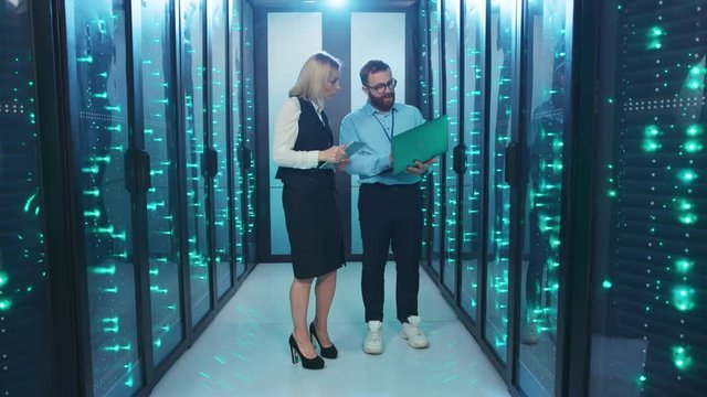 IT engineers man and woman inspecting supercomputer in secure server room. Team of professionals coworking in cyber security cloud computing and web hosting at data center.