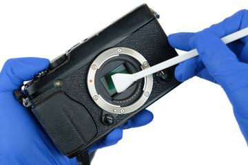 Hands cleaning digital mirrorless camera sensor from dust with swab
