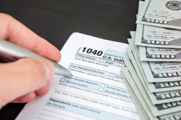 Obraz premium hand fills tax form 1040 on the background of dollars. Close-up. Business concept.