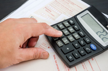 hand prints something on a calculator against the background of tax forms