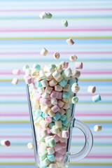 Marshmallows fall in mug. Small colorful marshmallows in glass mug on a striped background.