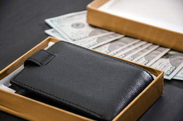 black, men's wallet in a box and dollars on a black background. Close-up.