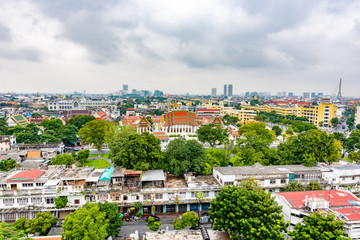 Panorama view of Bangkok city, Thailand. Cityscape of residental buildings in foreground, temples, skyscrapers and modern buildings in far. Fresh trees and plants. Cloudy weather, dramatic clouds.