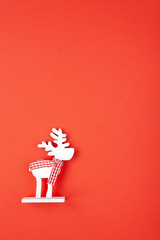 Christmas decoration, toy white deer in checkered scarf on red background, copy space. Festive, New Year concept. Vertical, flat lay. Minimal style. Top view