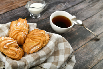 Choux cake with coffee on a wooden background. In a basket on a checkered towel. View from above. Chic with cottage cheese. Small custard cakes in wicker bowl on wooden background