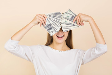 beautiful young woman in glasses on a beige background with dollars in hands
