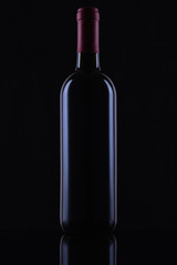 Black glass bottle of red wine on black background