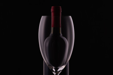 Red wine glass and a wine bottle with reflections on black background