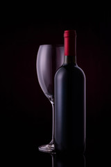Red wine glass and a wine bottle with reflections on black background