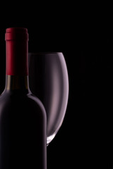 Red wine glass and a wine bottle with reflections on black background