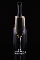 Abstract bottle champagne and glass with white sparkling wine on a black background. Festive concept.