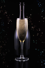 Bottle and glass of champagne on black background with golden bokeh circles. Place for text. Festive concept.