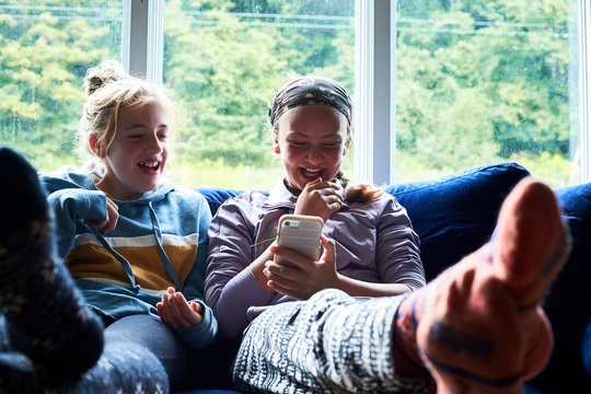 Teen girls laughing on a couch looking at something on a phone