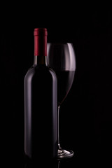 Elegant red wine glass and black wine bottle on black background