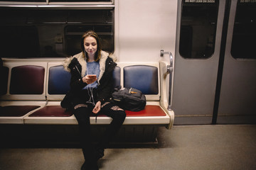 Young happy woman using smart phone while traveling in subway train