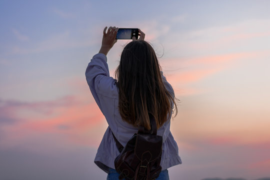 Young woman is taking a picture of the sky with her smartphone