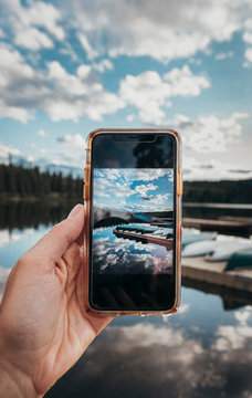Hand holding smartphone with image of scene in background on it.