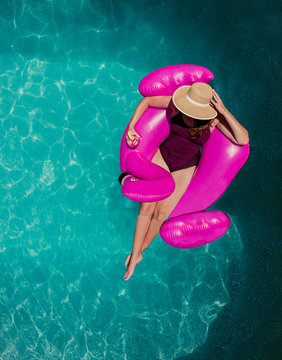 Top view of woman floating on inflatable pink flamingo in a pool.