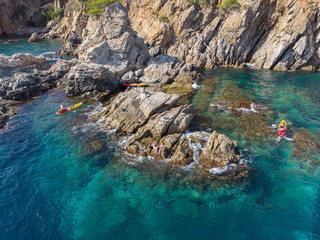Two women sitting on a rocky outcrop while people kayak nearby.