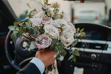 Groom carries a bouquet to the bride in a car close-up