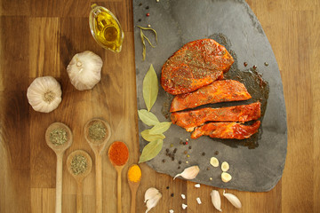 top view of raw, spices marinated in meat, lies on a black stone board on the table, garlic, bay leaf, potatoes and tomatoes nearby, cooking concept