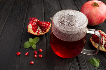 Pomegranate tea in the glass teapot on the black wooden background. Closeup.
