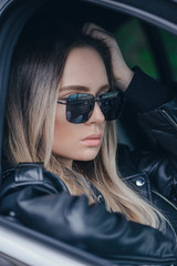 Stylish blonde woman in black sunglasses in car outdoor