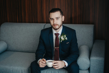 A man in a suit with a cup of coffee is sitting on a sofa looking at the frame.