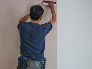 carpenter worker install wallpaper on white wall