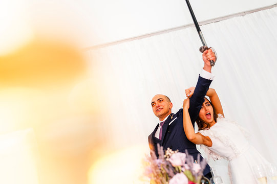Exited couple of newly weds raising a sword to cut the wedding cake
