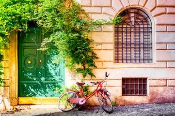 Fototapeta na wymiar Old house wall in Trastevere, Rome, Italy with a red bicycle and green door. Old cozy street in Rome