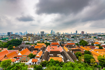 Panorama view of Bangkok city, Thailand. Cityscape of residental buildings in foreground, temples, skyscrapers and modern buildings in far. Fresh trees and plants. Cloudy weather, dramatic clouds.