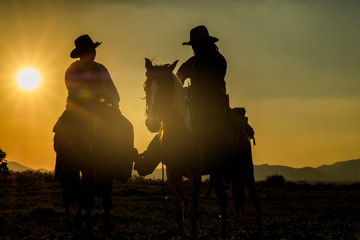 Two cowboys riding horseback at sunset with yellow sky
