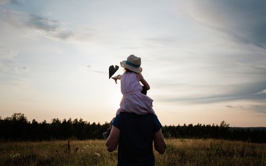 father carrying his daughter on his shoulders in a meadow at sunset