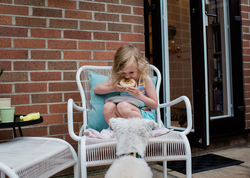 girl eating outside whilst her dog looks longingly for food