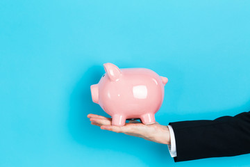 Businessman holding a pink piggy bank on a blue background