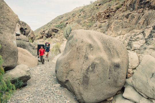 Two male climbers walk by boulders in the desert