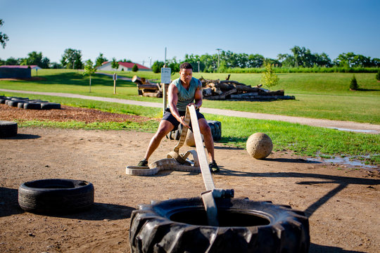 An athletic firefighter tugs a heavy tire with a length of firehose