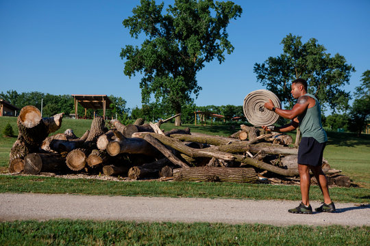 An athletic man prepares to throw a roll of heavy firehose in a park