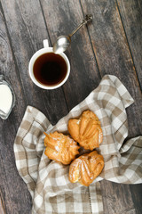 Choux cake with coffee on a wooden background. In a basket on a checkered towel. View from above. Chic with cottage cheese. Small custard cakes in wicker bowl on wooden background