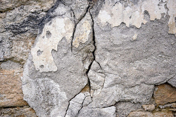 Cracked and crumbling stucco on the wall of wild stone. Deep and winding crack. Close-up. Selective focus.