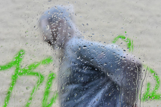 Man wearing raincoat passing in front of a car with rain drops