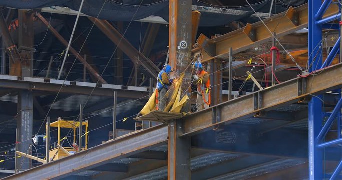Two construction workers welding steel structural beams on a high rise building site
