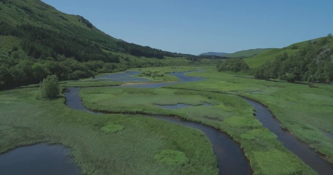 Low aerial flying over the lush green grass and water networks of Loch Dochart in the Scottish Highlands in classic Highland setting
