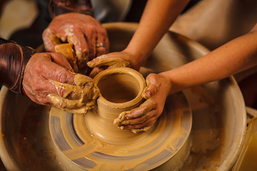 A close-up of the hand of a male potter who teaches his pupil, a child of the art of making a pot or a vase of clay. People working on potters.