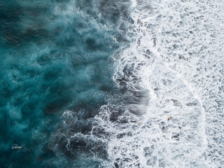 Aerial view of ocean surface, waves, white water and surfers