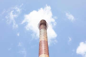 High brick industrial chimney on blue sky background. Small cloud on top. Red and white colors. Old...