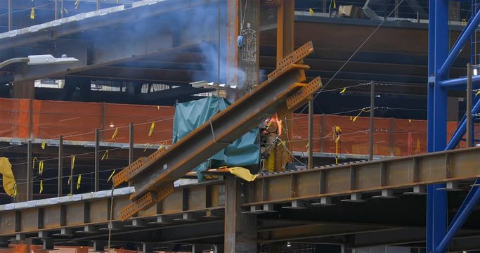 Construction worker welding steel structural beams on site with sparks and smoke