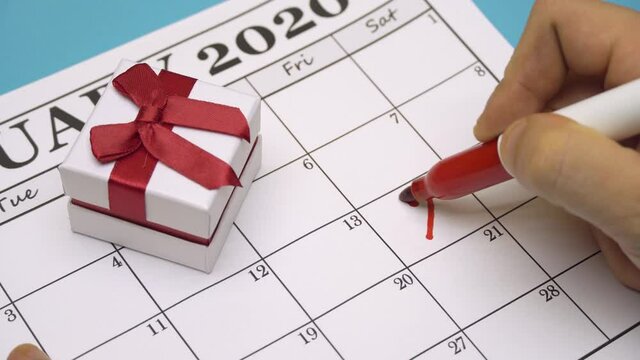 male Hand with a red marker will draw a heart shape on the calendar February 14 near the gift. Valentine's Day